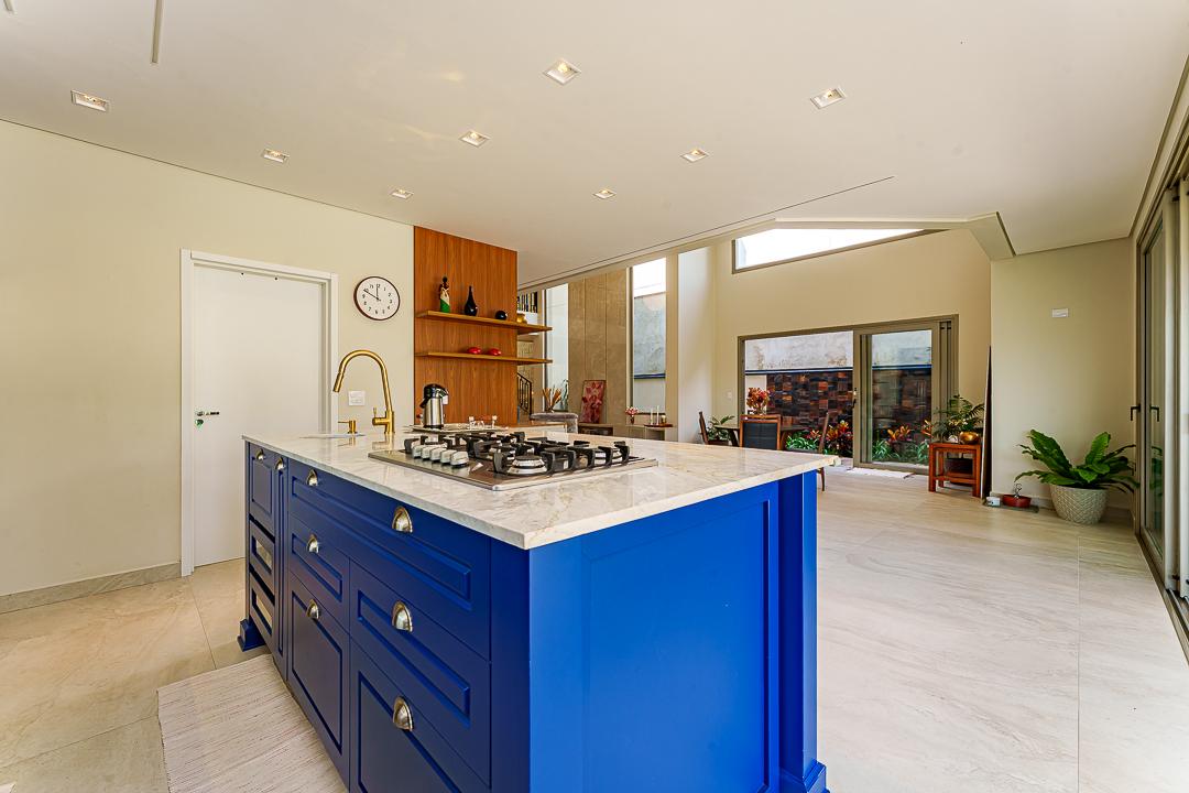 Ilha da cozinha da Casa X-18 com bancada de mármore Branco Paraná, cooktop embutido e marcenaria azul